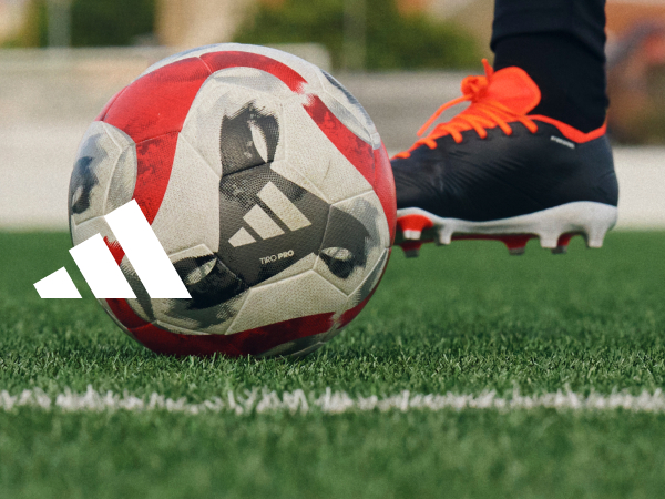 adidas soccer cleat kicking an adidas soccer ball on turf. White adidas logo.